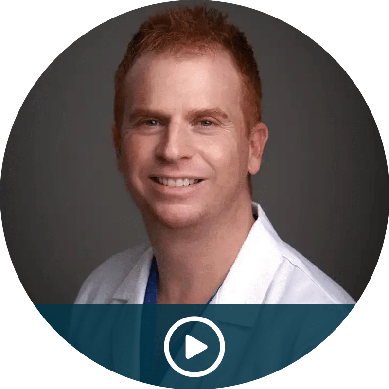 Smiling man in a white coat portrait with a play button indicating a video thumbnail.