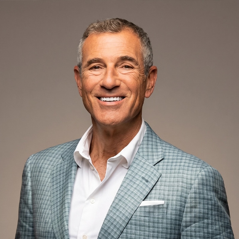 Smiling man in a light blue checkered blazer and white shirt, looking at the camera.