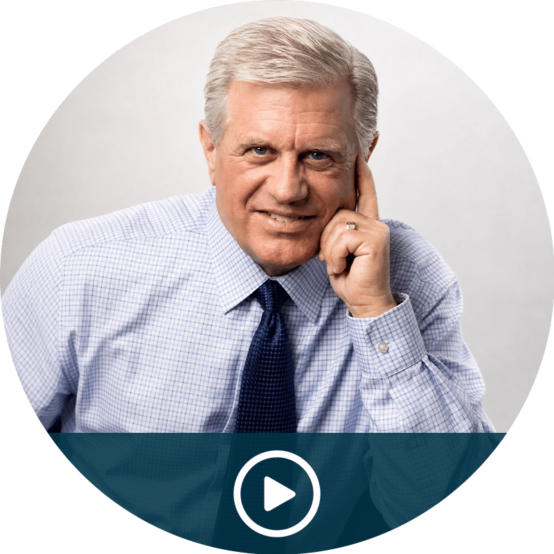 Video thumbnail: smiling gray-haired man in a blue dress shirt and tie, ready to play.