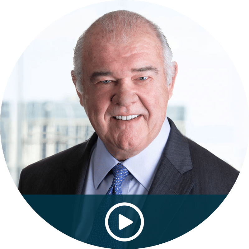 Video thumbnail: smiling older man in a dark suit and blue tie; click to play.