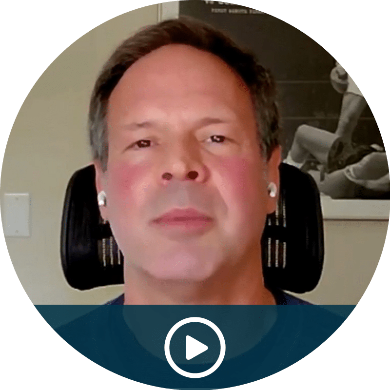 Video thumbnail showing a man speaking, seated in a chair, with a play button overlay at the bottom center.