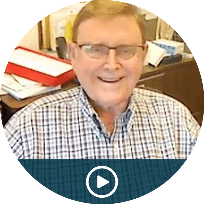 Video thumbnail: smiling man in a checkered shirt and glasses in an office, with a play button overlay at the bottom edge.